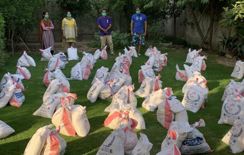 Photo: image of bags of donations gathered and distributed by URI members during the COVID-19 pandemic with 4 people standing nearby