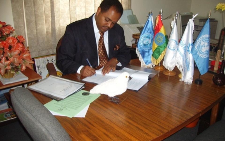 Mussie Hailu, singing documents at his desk  