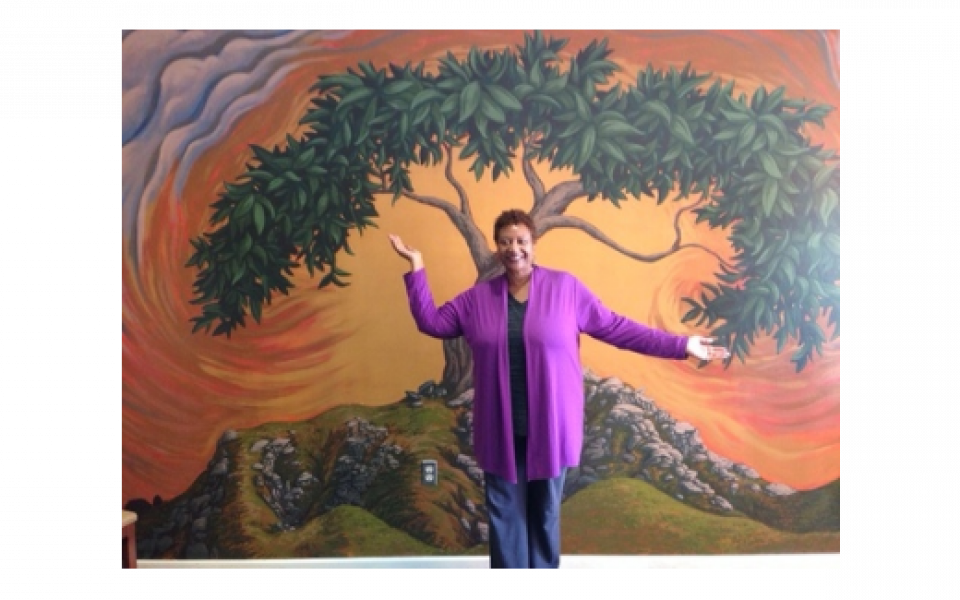 Photo: An image of Reverend Wilkins standing in front of a mural depicting a tree